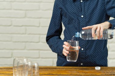 Çocuk plastik şişeden ahşap masadaki cama su döküyor.