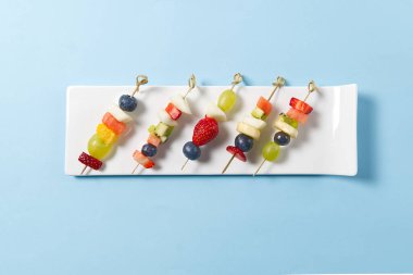 Bambu şiş üzerinde taze yaz meyveleri, mavi üzerinde izole