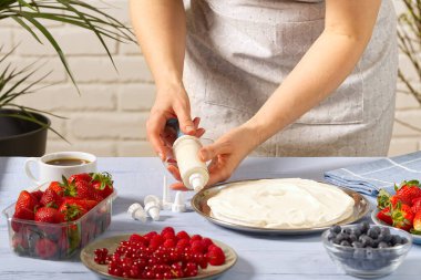 Kadın fırıncı krem şanti sıkar. Kremalı pasta ve çilekli kremadan yapılmış ev yapımı çilekli pasta..