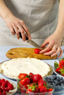 Kadın fırıncı çilekli pasta için çilek keser. Kremalı pasta ve çilekli kremadan yapılmış ev yapımı çilekli pasta..