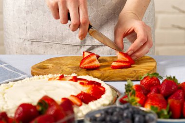 Kadın fırıncı çilekli pasta için çilek keser. Kremalı pasta ve çilekli kremadan yapılmış ev yapımı çilekli pasta..