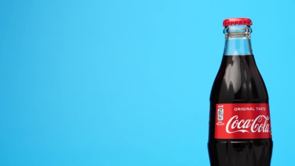 Estonia, Tallin - Marzo 2021: botella de vidrio bebida de coca-cola de soda girando sobre fondo azul aislado. — Vídeo de stock