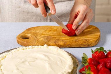 Kadın fırıncı çilekli pasta için çilek keser. Kremalı pasta ve çilekli kremadan yapılmış ev yapımı çilekli pasta..