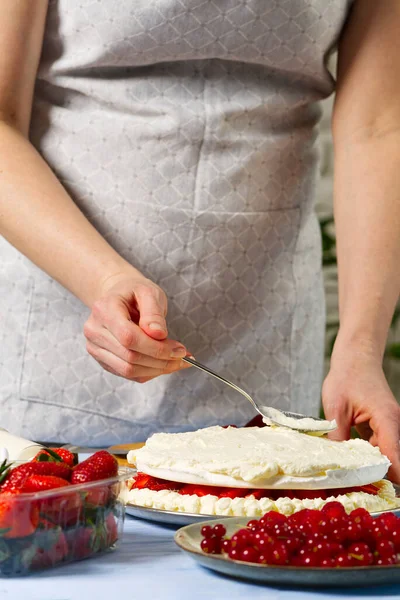 Woman baker adds whipped cream to the strawberry cake. Homemade strawberries cake made from meringue cake and cream with strawberries. Royalty Free Stock Images