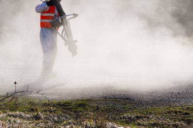 Asfalt yolun hızlı bahar tamiri. Hızlı onarım sırasında üniformalı bir işçi. granit ezilmiş taş ve erimiş katran, zift.