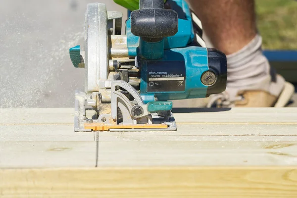 worker sawing wood board with electric circular saw. Carpenter working with a circular saw outside in sunny day. close-up