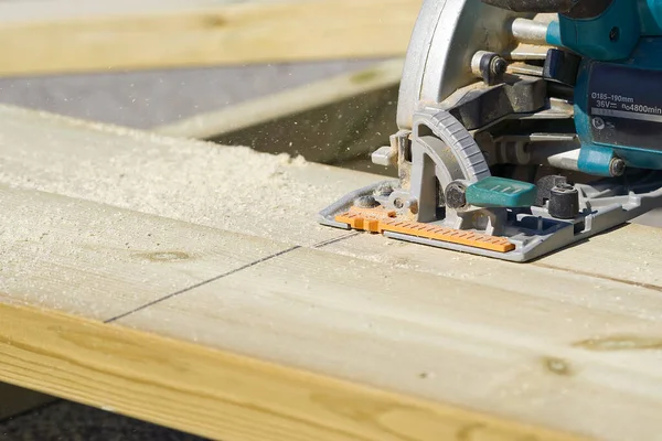 worker sawing wood board with electric circular saw. Carpenter working with a circular saw outside in sunny day. close-up