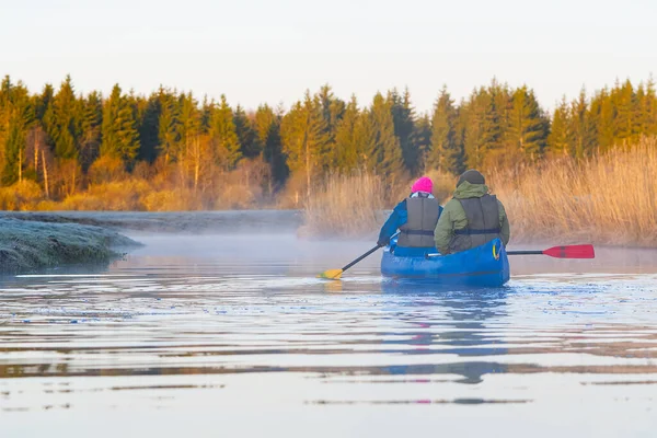 Retirees rowing a canoe in early spring in the early morning. seniors lifestyle. Morning landscape, fog by the morning river and people on the canoe — Stock Photo, Image