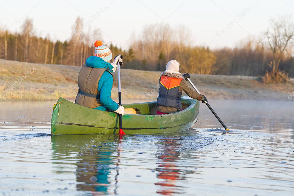 mother and daughter rowing a canoe in early spring in the early morning. active lifestyle. Morning landscape, fog by the morning river and people on the canoe
