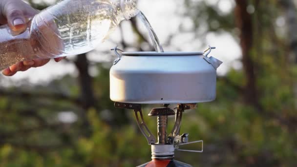 Napełnianie czajnika kempingowego wodą z plastikowej butelki. aluminiowy czajnik do wędrówek po palniku gazowym — Wideo stockowe