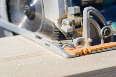 Elektrikli testere ile tahta testeresi kesen bir işçi. Marangoz güneşli bir günde dışarıda dairesel bir testereyle çalışıyor. yakın plan