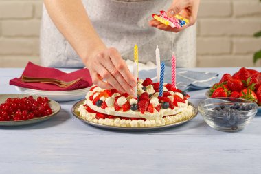 Kadın eli, ev yapımı çilekli keke doğum günü mumları ekliyor. Çilekli turta ve doğum günü mumları.