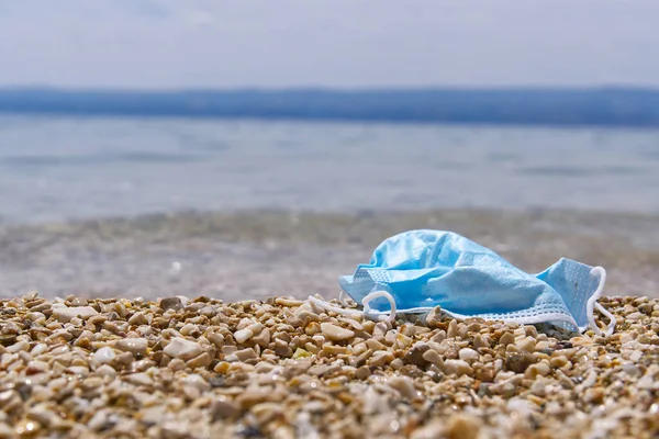 La mascarilla médica azul se encuentra en la playa. Contaminación plástica ambiental y costera durante las pandemias de covid-19 — Foto de Stock
