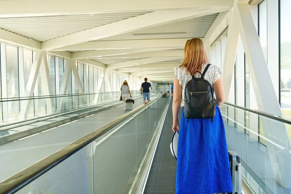 Mladá čtyřicátnice nemá obličej s kufříkem na eskalátoru na letištním terminálu. Bezpečnost cestování sám Covid-19 čas — Stock fotografie