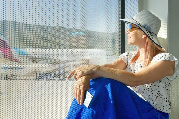 Hezká žena čeká na odlet na letišti. žena dáma cestující sedí na patře v blízkosti okna s výhledem na dráhu — Stock fotografie