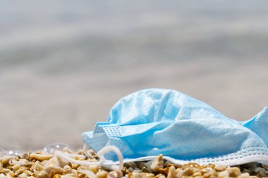 Plajda duran mavi tıbbi maske kullanılmış. Covid-19 salgınları sırasında çevre ve sahil plastik kirliliği