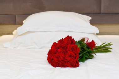 Balayı için bir otel odasında yatağın üzerinde kırmızı güller. Otelde konuklarla romantik bir buluşma..