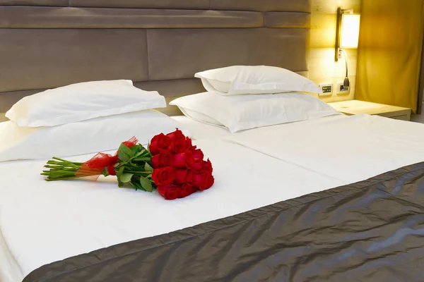 Букет красных роз на кровати в номере отеля на медовый месяц. романтическая встреча гостей в отеле. — стоковое фото