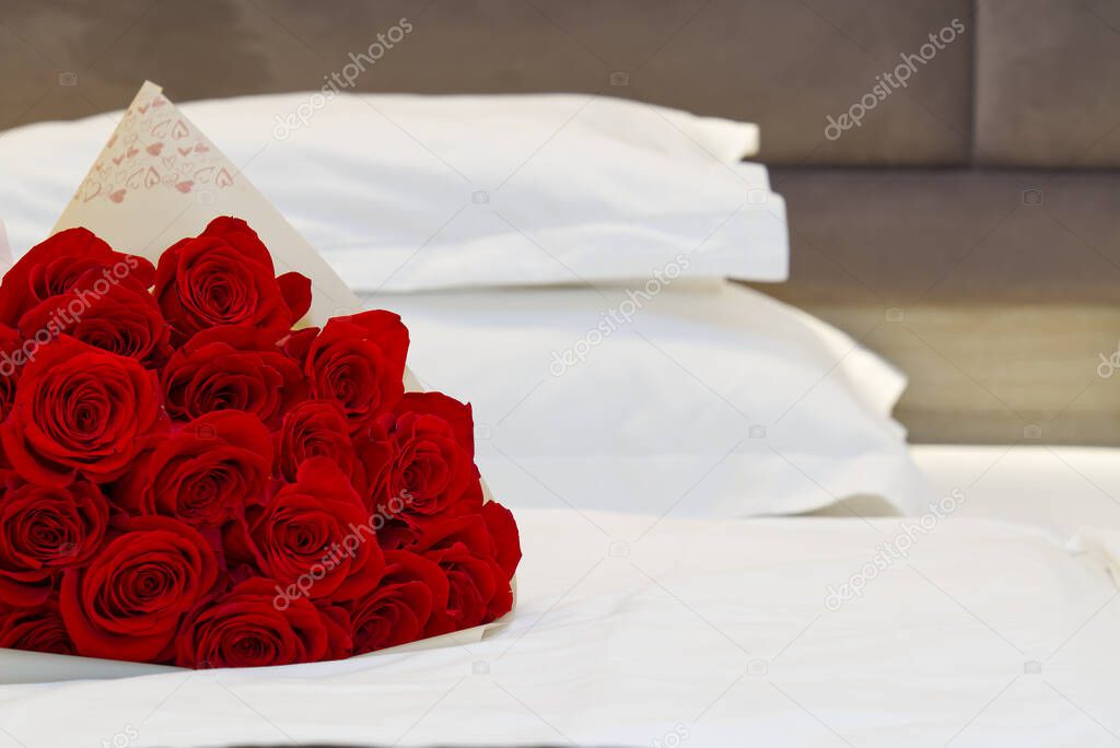 bouquet of red roses on the bed in a hotel room for honeymoon. romantic meeting of guests at the hotel.