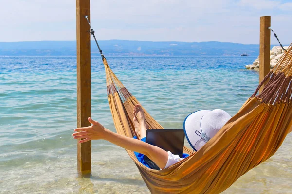 Work from anywhere. Young smilyng woman, female freelancer in straw hat working on laptop on beach.