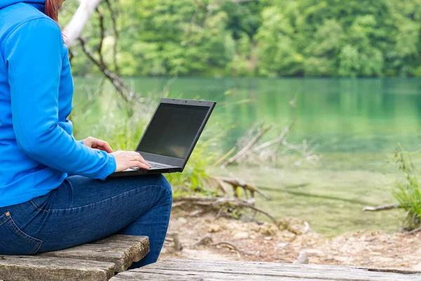 Jovem, freelancer do sexo feminino trabalhando com laptop com bela vista da floresta e lago. — Fotografia de Stock