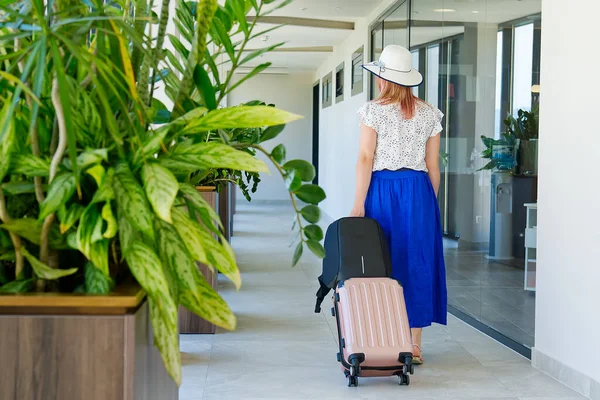 Dívka turista odbaví z hotelu. Turista s kufrem procházky po chodbě v hotelu — Stock fotografie