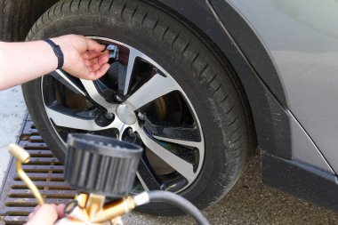 Şoför benzin istasyonunda bir arabanın tekerleğini şişiriyor.