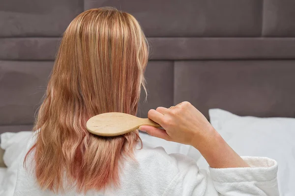 Una rubia con el pelo teñido peinándose el pelo enredado después de una ducha con un peine de madera. —  Fotos de Stock