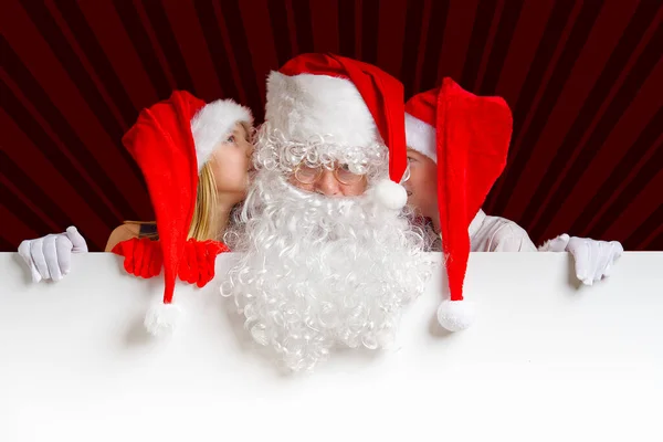 Satna claus mit lustigen Kindern in roten Weihnachtszwergenhüten, die hinter einem weißen Transparent hervorlugen — Stockfoto