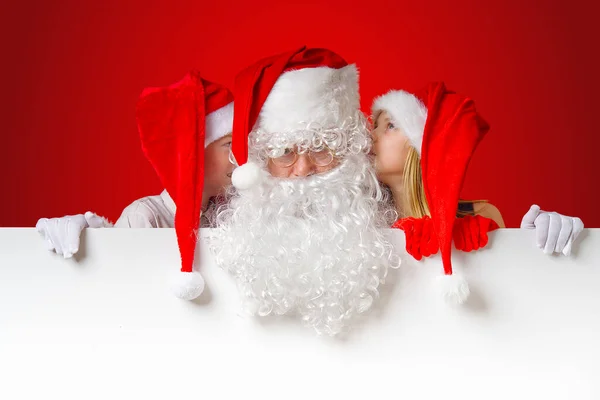 Satna claus vicces gyerekek piros karácsonyi törpe kalap kukucskál ki mögül egy üres fehér banner — Stock Fotó