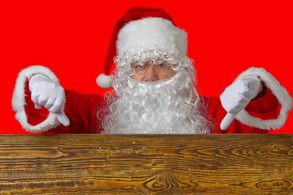 Portrait of a cheerful santa claus peeking out from behind a brown wooden shield — Stock Photo, Image