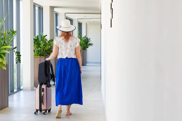 Dívka turista odbaví z hotelu. Turista s kufrem procházky po chodbě v hotelu — Stock fotografie