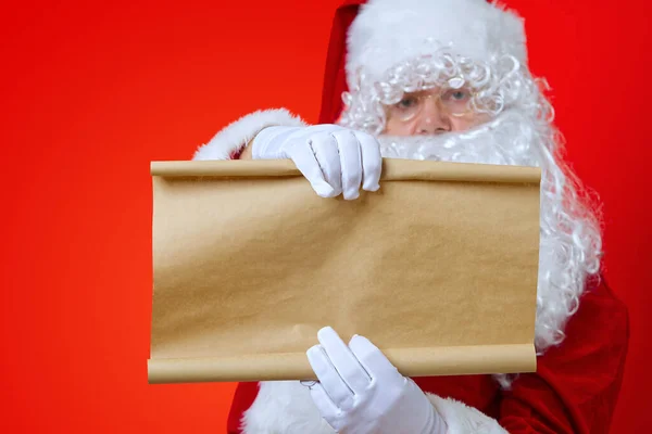 Papai Noel segurando papel de pergaminho marrom em branco. Natal feriado lista de desejos conceito mockup — Fotografia de Stock