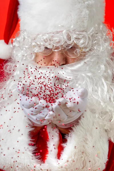 Papai Noel soprando vermelho glitter confetti de mãos — Fotografia de Stock