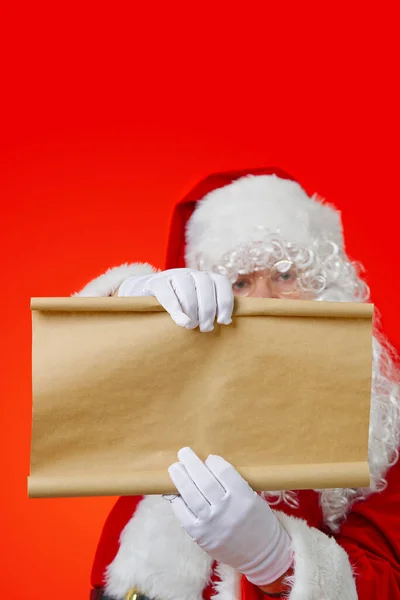 Santa Claus holding blank brown scroll paper. Christmas holiday wish list concept mockup — Stock Photo, Image