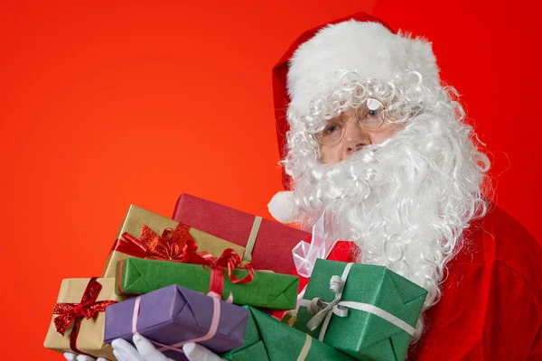 Feliz Papai Noel com caixas de presente em mãos no fundo vermelho com espaço de cópia — Fotografia de Stock