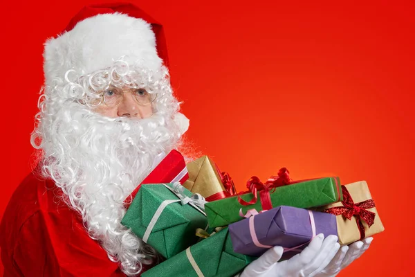 Feliz Papai Noel com caixas de presente em mãos no fundo vermelho com espaço de cópia — Fotografia de Stock