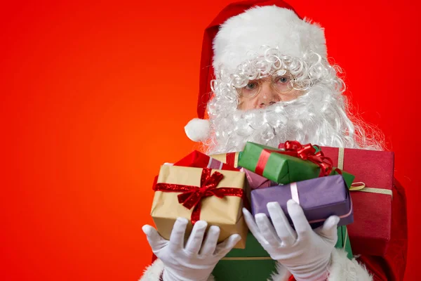 Szczęśliwy Święty Mikołaj z pudełek w rękach na czerwonym tle z miejsca do kopiowania — Zdjęcie stockowe