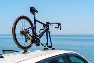 Şık bir bisiklet, bir arabanın tavan rafına monte edilir. Parlak denizin göz kamaştırıcı zeminine ve parlak mavi gökyüzüne karşı kurulur. Macera duyguları ve seyahat heyecanı uyandırır..