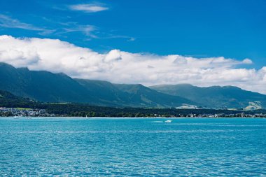 Sakin bir alp gölü, görkemli dağlarla çevrili mavi gökyüzünü ve bulutları yansıtır. Bu sakin manzara doğa, seyahat ve turizm temaları için mükemmeldir..