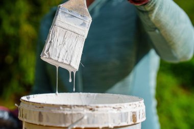 Bir ressamın çalışma alanı açık bir kabın içine damlayan beyaz boyayla dolu bir fırça içerir, DIY projelerini, ev geliştirmeyi veya tasarım kavramlarını göstermek için idealdir.