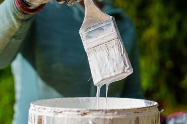 Yakından bakınca boya kaplı bir fırçanın tenekeye fazla beyaz boya damlattığını görüyoruz. Bu resim, bir ev yenileme projesi için hazırlanmanın özünü yansıtıyor..