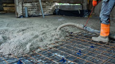 Islak çimentoyu takviye ağının üzerine ustalıkla döşeyen bir inşaat işçisi. Bu resim inşaat süreçlerini, döşeme projelerini ve bina yenileme temellerini temsil ediyor.