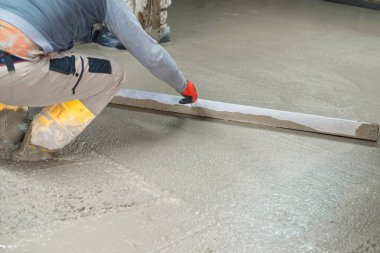 Bir inşaat işçisi düz bir yüzey sağlamak için düz bir araç kullanarak beton zemini düzleştirir. Bu resim, inşaattaki kaliteli işçiliğe olan bağlılığı vurgular.