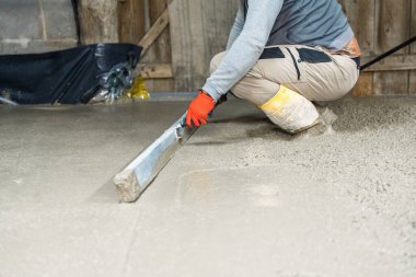 Becerikli bir zanaatkar, yeni dökülmüş beton bir yüzeyi bir el aleti, hassasiyet ve zanaatkarlık göstererek yerle bir eder. Bu resim, inşaatta pürüzsüz bir bitirme tekniğini vurgular.