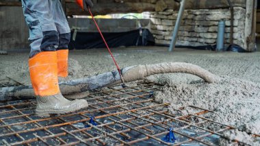Bir inşaat işçisi beton dökerek temel oluşturur. Takviye ağlar güç katar ve bu önemli inşaat sırasında güvenlik botları işçileri korur..