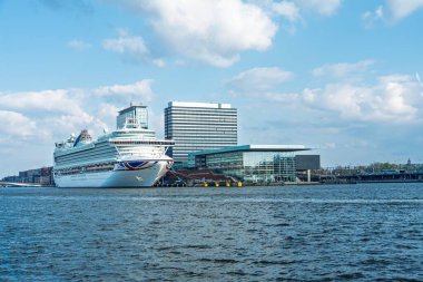 Amsterdam 'ın cazibesini, modern mimarinin parlak gökyüzü altındaki görkemli bir yolcu gemisi manzarasıyla keşfedin. Seyahat broşürleri ve turizm promosyonları için mükemmel.