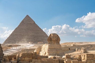 Sfenks ve Giza Piramidi kabarık bulutlu mavi gökyüzüne karşı görkemli bir şekilde yükselir. Bu ikonik görüntü antik Mısır medeniyetinin ihtişamını yansıtır. Seyahat ve tarih için mükemmeldir..