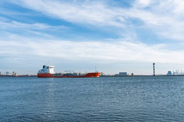 Bir turuncu tanker, ince bulutlu bir gökyüzünün altında sakin mavi okyanus sularında süzülür. Bu sahne küresel ticaret, deniz taşımacılığı ve endüstriyel faaliyet temalarını yakalar.