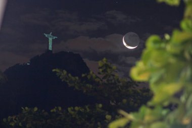 Kurtarıcı İsa ve Brezilya, Rio de Janeiro 'daki hilal ayı - 15 Mayıs 2021: Cristo Redentor yakınlarındaki ay batımı, Copacabana' nın manzarası.